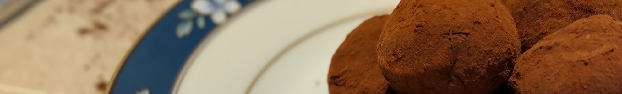 Handmade chocolate truffles on a blue plate with a spoon of cocoa powder