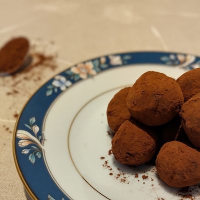 Handmade chocolate truffles on a blue plate with a spoon of cocoa powder