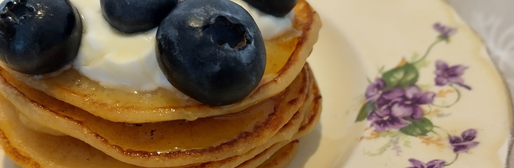 Stack of golden pancakes topped with yoghurt, honey and blueberries