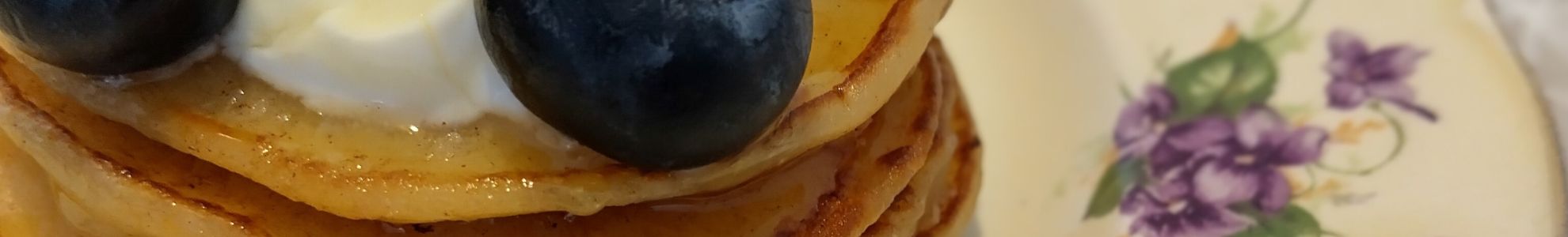 Stack of golden pancakes topped with yoghurt, honey and blueberries