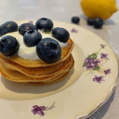 Stack of golden pancakes topped with yoghurt, honey and blueberries